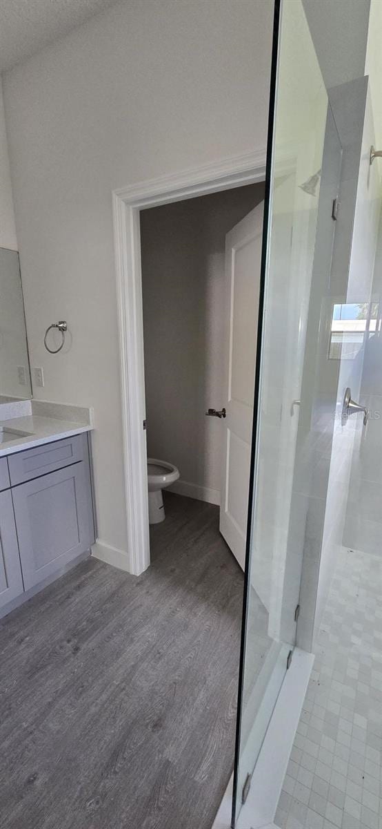 bathroom with a shower stall, vanity, toilet, wood finished floors, and baseboards