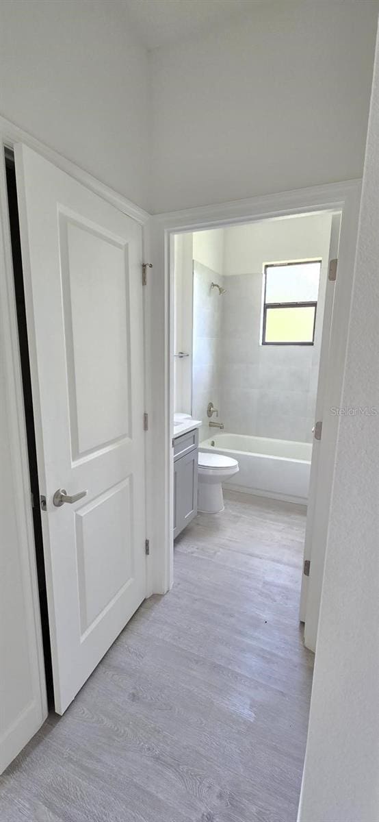 bathroom featuring wood finished floors, washtub / shower combination, vanity, and toilet