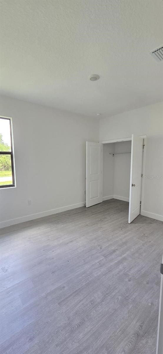 unfurnished bedroom featuring baseboards, wood finished floors, a textured ceiling, and a closet