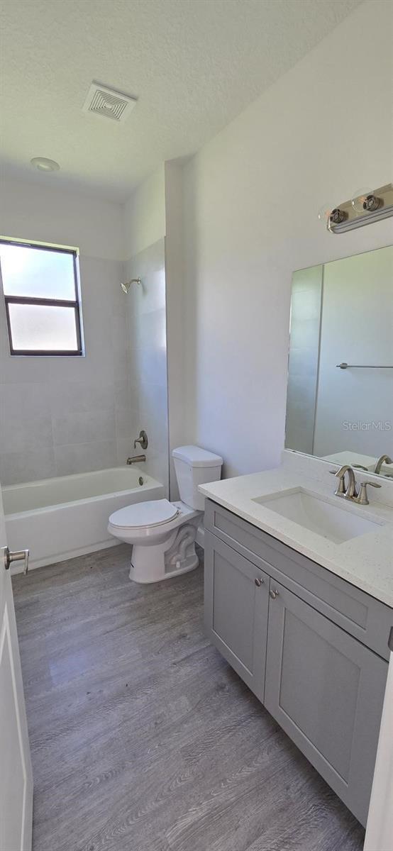 full bath with toilet, tub / shower combination, wood finished floors, and vanity