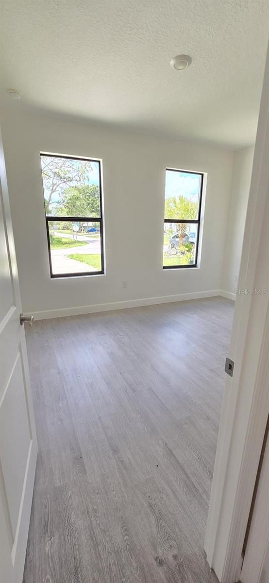 spare room featuring healthy amount of natural light, wood finished floors, a textured ceiling, and baseboards