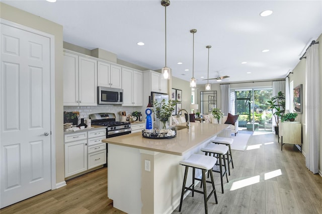 kitchen with appliances with stainless steel finishes, a sink, light wood finished floors, decorative backsplash, and a breakfast bar area