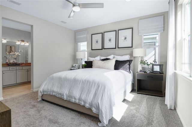 bedroom featuring light colored carpet, ensuite bathroom, ceiling fan, and baseboards