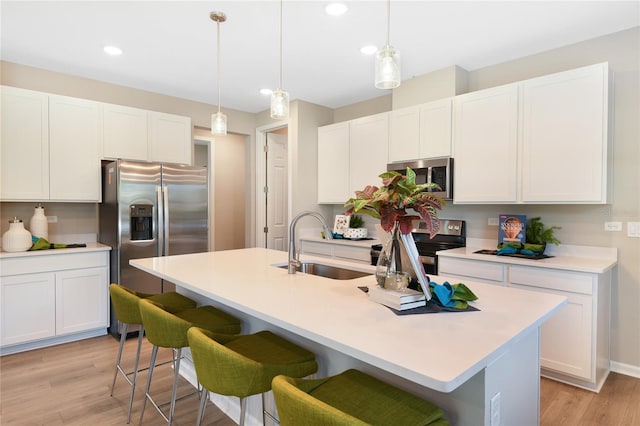 kitchen with appliances with stainless steel finishes, a sink, recessed lighting, light wood-type flooring, and white cabinets