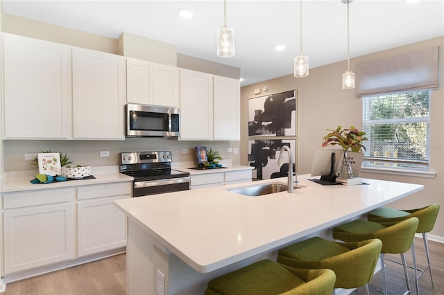 kitchen with appliances with stainless steel finishes, a sink, light wood-style floors, a kitchen island with sink, and recessed lighting