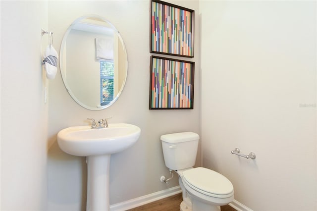 half bath featuring baseboards, toilet, a sink, and wood finished floors