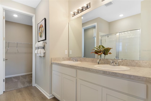 full bath with a stall shower, a walk in closet, wood finished floors, double vanity, and baseboards