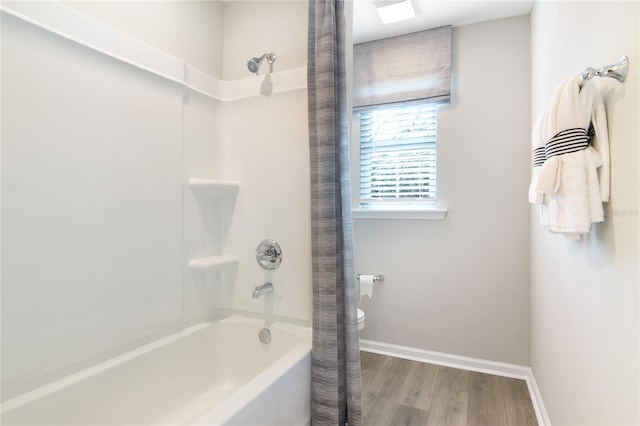 bathroom featuring baseboards, wood finished floors, and shower / bath combo