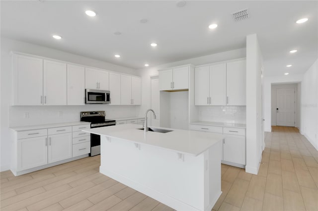 3723 Malad Way, Tavares, FL 32778 - kitchen featuring stainless steel appliances, an island with sink, decorative backsplash, white cabinets, and light countertops