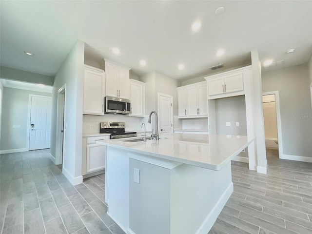 1001 Umbria Dr, Poinciana, FL 34759 - kitchen with stainless steel appliances, white cabinetry, a center island with sink, wood finish floors, and light countertops