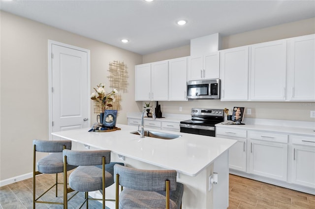 9253 Players Dr, Weeki Wachee, FL 34613 - kitchen featuring stainless steel appliances, a sink, light wood-style floors, an island with sink, and white cabinetry