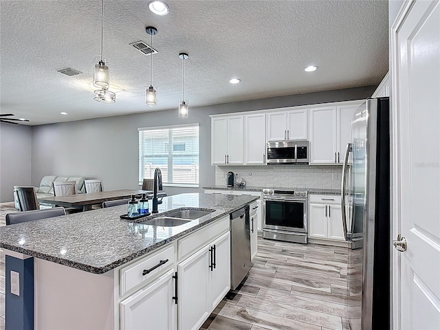 140 Trinity Ridge Cir, Davenport, FL 33897 - kitchen with stainless steel appliances, a sink, light wood-style floors, white cabinets, and a center island with sink
