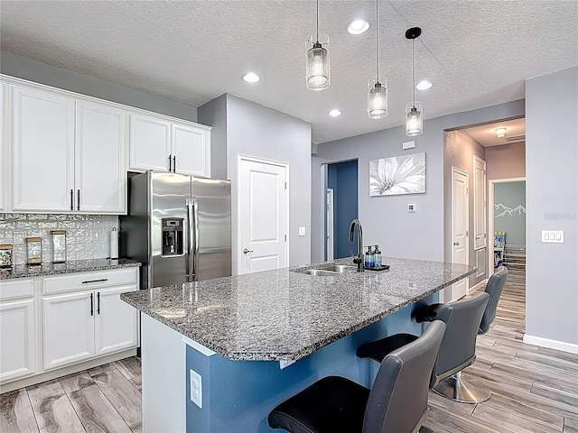 140 Trinity Ridge Cir, Davenport, FL 33897 - kitchen featuring stainless steel refrigerator with ice dispenser, light wood-type flooring, white cabinetry, a breakfast bar, and dark stone counters