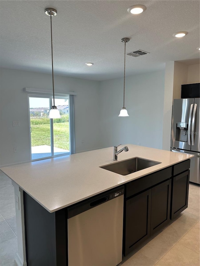 kitchen featuring stainless steel appliances, a sink, light countertops, a kitchen island with sink, and hanging light fixtures
