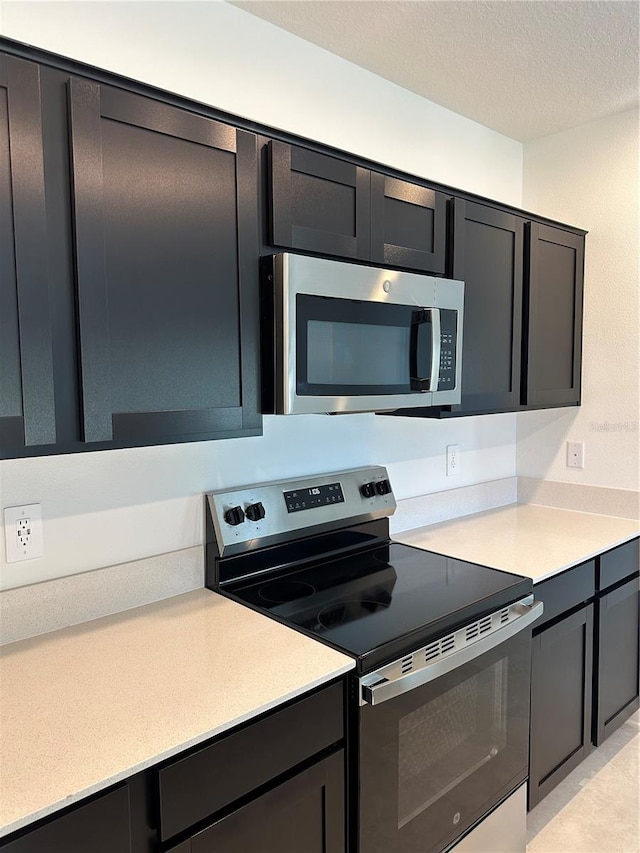 kitchen with appliances with stainless steel finishes, light countertops, dark cabinetry, and a textured ceiling