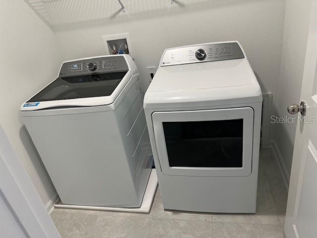 clothes washing area with washer and dryer and light tile patterned floors