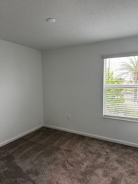 spare room featuring dark colored carpet and baseboards