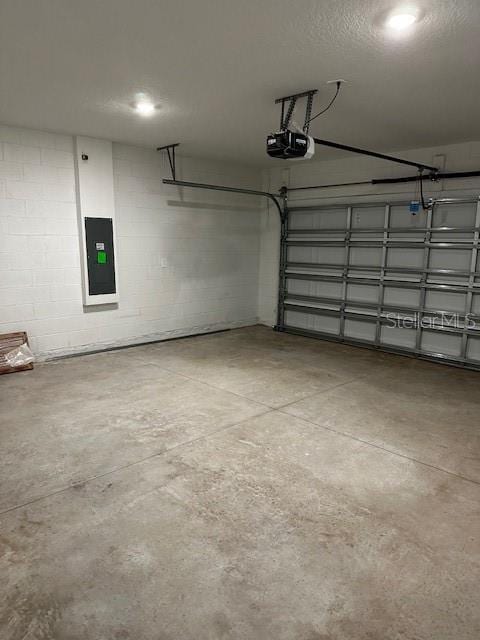 garage featuring a garage door opener, electric panel, and concrete block wall
