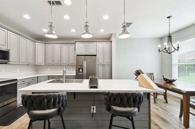 1272 Bonita Canyon Dr, Kissimmee, FL 34759 - kitchen with appliances with stainless steel finishes, a sink, a kitchen breakfast bar, light wood-style floors, and a chandelier