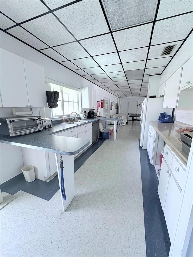 870 Virginia St Unit 108, Dunedin, FL 34698 - kitchen featuring white cabinets, stainless steel dishwasher, a sink, a paneled ceiling, and a peninsula