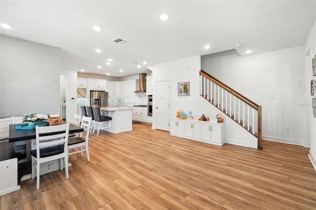 7400 Estuary Lake Loop, Celebration, FL 34747 - kitchen featuring stainless steel fridge with ice dispenser, a breakfast bar area, backsplash, light wood-style floors, and wall chimney range hood