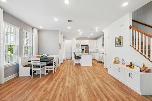7400 Estuary Lake Loop, Celebration, FL 34747 - kitchen with stainless steel fridge with ice dispenser, a kitchen breakfast bar, light wood-style floors, white cabinetry, and decorative backsplash