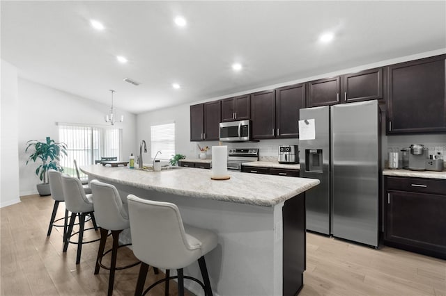 1524 Fleur Dr, Davenport, FL 33837 - kitchen with stainless steel appliances, a kitchen bar, an island with sink, vaulted ceiling, and light wood-style floors