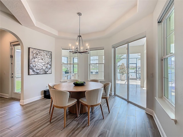 1211 Terralago Way, Kissimmee, FL 34746 - dining room with a tray ceiling, wood finished floors, a chandelier, arched walkways, and baseboards