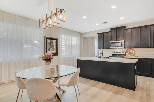 8042 Glenlloyd Ave, Winter Garden, FL 34787 - kitchen featuring stainless steel appliances, a sink, a center island with sink, light wood-style flooring, and light countertops