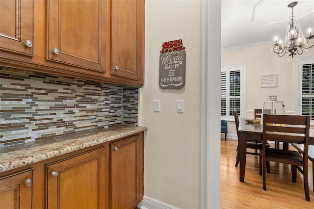 3349 Schoolhouse Rd, Harmony, FL 34773 - kitchen featuring brown cabinetry, decorative backsplash, a chandelier, light wood-type flooring, and crown molding