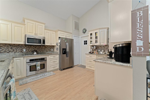 2507 Talega Dr, Saint Cloud, FL 34772 - kitchen with stainless steel appliances, cream cabinetry, backsplash, light stone counters, and high vaulted ceiling