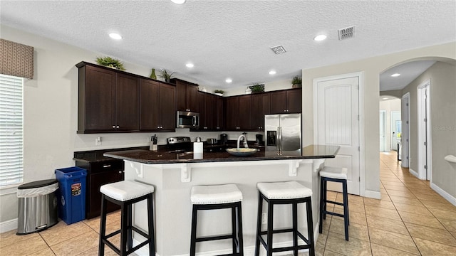 1228 Castle Pines Ct, Reunion, FL 34747 - kitchen with appliances with stainless steel finishes, light tile patterned flooring, a kitchen breakfast bar, dark brown cabinets, and a textured ceiling