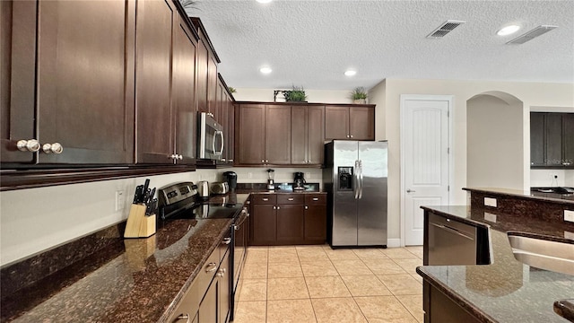 1228 Castle Pines Ct, Reunion, FL 34747 - kitchen featuring stainless steel appliances, dark brown cabinetry, dark stone countertops, arched walkways, and light tile patterned flooring