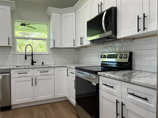 814 Gator Ln, Deltona, FL 32738 - kitchen featuring appliances with stainless steel finishes, a sink, backsplash, white cabinetry, and wood finished floors