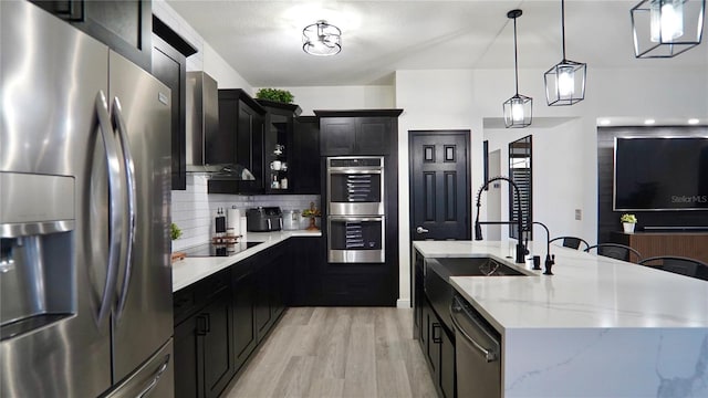 1025 Belvoir Dr, Kissimmee, FL 34744 - kitchen with stainless steel appliances, dark cabinetry, wall chimney exhaust hood, and light wood finished floors
