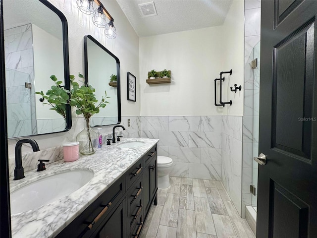 1025 Belvoir Dr, Kissimmee, FL 34744 - full bathroom with tile walls, a textured ceiling, a shower stall, toilet, and double vanity