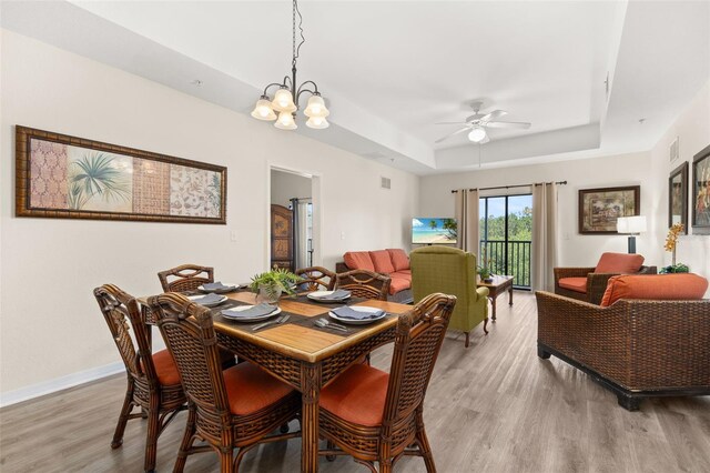 9055 Treasure Trove Ln Unit 409, Kissimmee, FL 34747 - dining area featuring a tray ceiling, light wood-style flooring, a ceiling fan, baseboards, and a chandelier