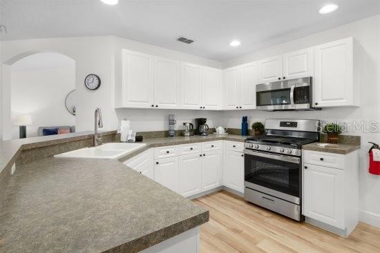 252 Barbera Dr, Davenport, FL 33897 - kitchen with stainless steel appliances, arched walkways, white cabinetry, recessed lighting, and light wood finished floors