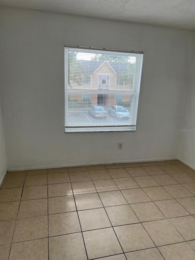 empty room with healthy amount of natural light, light tile patterned flooring, baseboards, and a textured ceiling