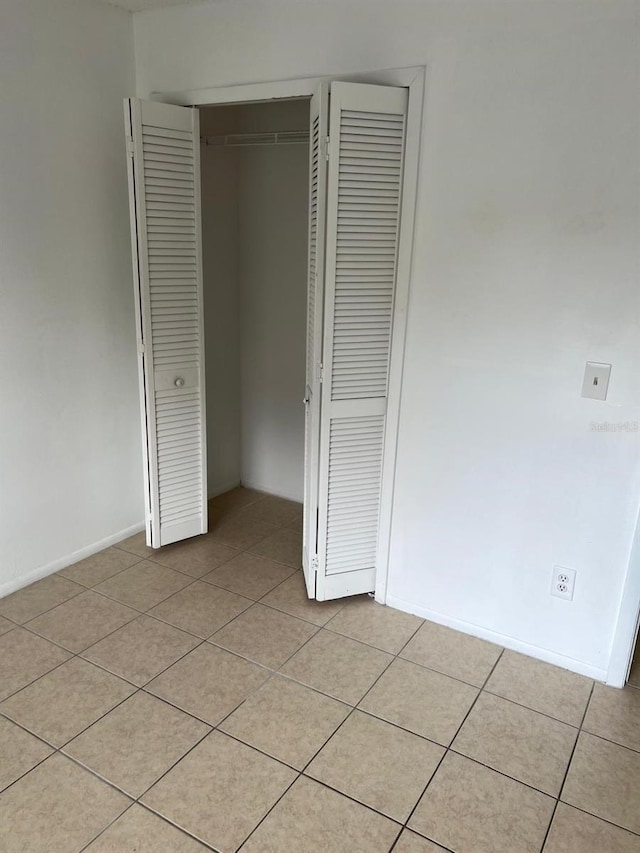 unfurnished bedroom featuring a closet, light tile patterned flooring, and baseboards