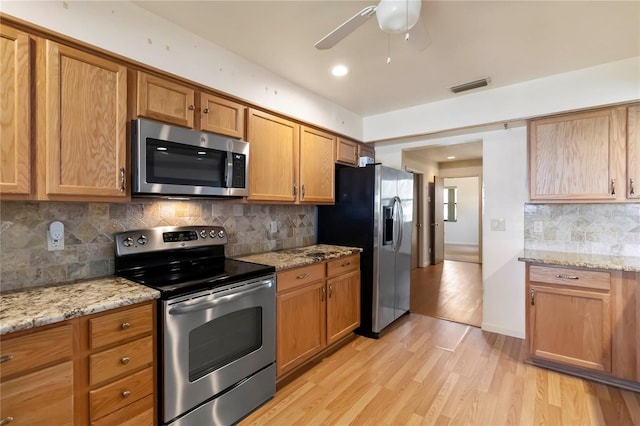 2740 Barker Rd, Saint Cloud, FL 34771 - kitchen featuring appliances with stainless steel finishes, ceiling fan, decorative backsplash, light wood-type flooring, and light stone countertops