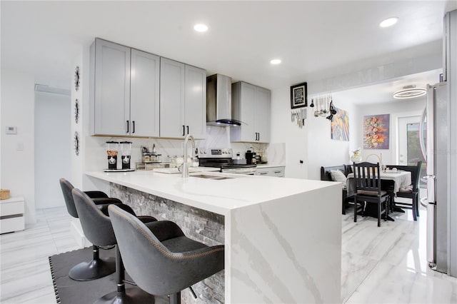 416 E Seminole Ave, Lake Wales, FL 33853 - kitchen with wall chimney exhaust hood, gray cabinets, stainless steel appliances, decorative backsplash, and light stone counters