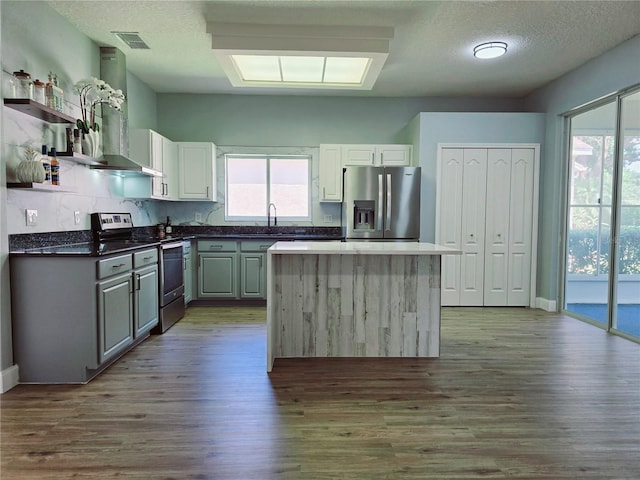 2312 Twickingham Ct, Clermont, FL 34711 - kitchen featuring stainless steel appliances, open shelves, wall chimney exhaust hood, wood finished floors, and a textured ceiling