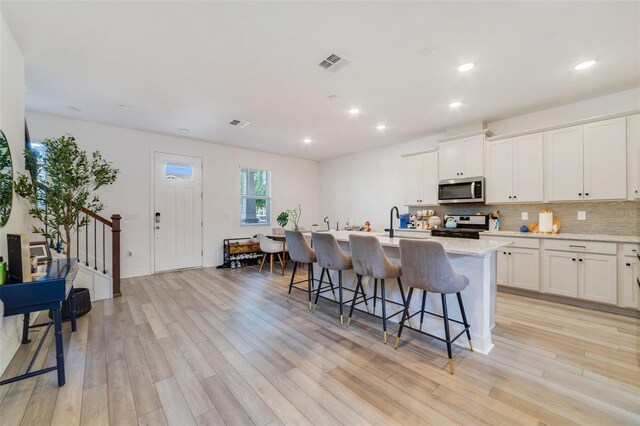2224 Celebration Blvd, Celebration, FL 34747 - kitchen featuring appliances with stainless steel finishes, light wood-style floors, a breakfast bar, a kitchen island with sink, and decorative backsplash