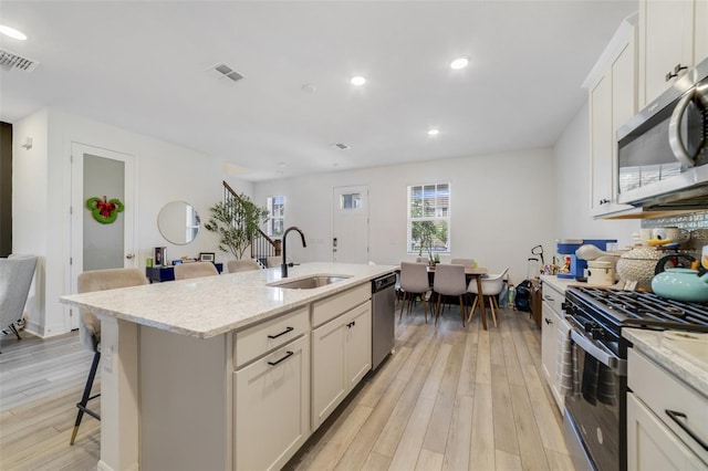 2224 Celebration Blvd, Celebration, FL 34747 - kitchen featuring a sink, appliances with stainless steel finishes, light wood-style floors, a kitchen bar, and a kitchen island with sink
