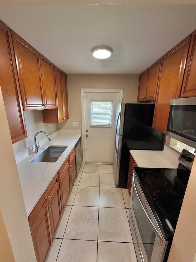 1001 Plantation Dr Unit E1, Kissimmee, FL 34741 - kitchen with stainless steel appliances, a sink, brown cabinetry, light stone counters, and light tile patterned floors