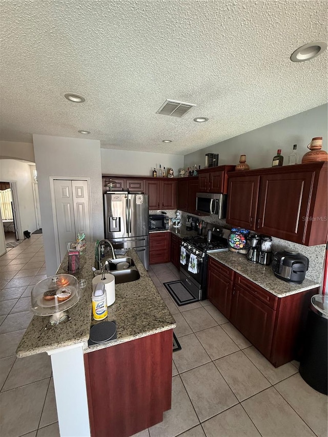 939 Jaybee Ave, Davenport, FL 33897 - kitchen with stainless steel appliances, a sink, light tile patterned floors, a center island with sink, and a textured ceiling