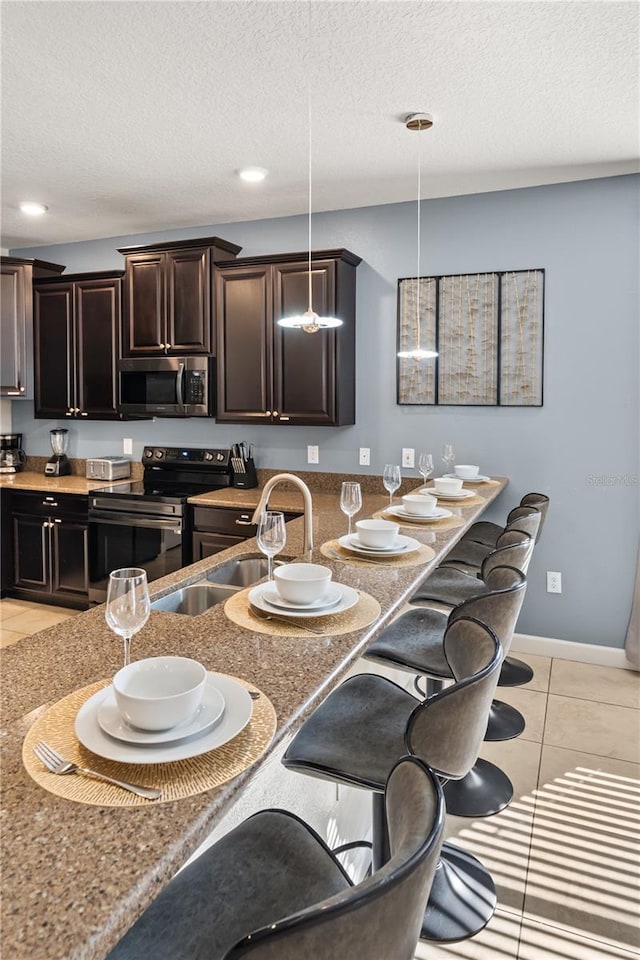 1456 Belle Terre Rd, Davenport, FL 33896 - kitchen with appliances with stainless steel finishes, a kitchen breakfast bar, light tile patterned floors, a textured ceiling, and dark brown cabinetry