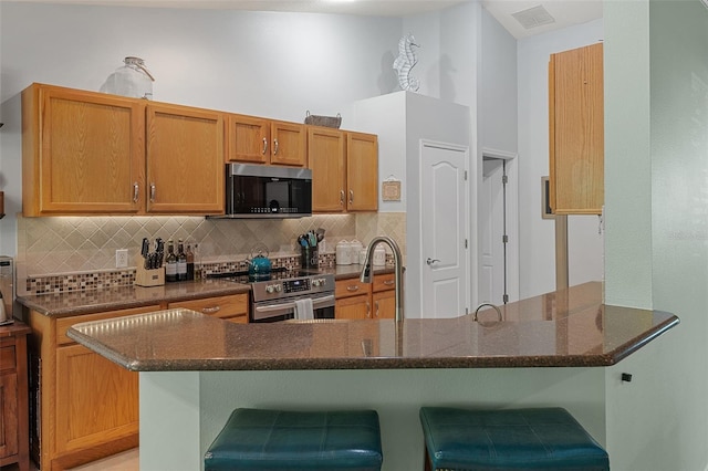 1523 Stafford Ave, Merritt Island, FL 32952 - kitchen featuring appliances with stainless steel finishes, backsplash, dark stone countertops, a kitchen bar, and a peninsula