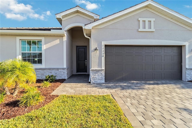 11330 Burgundy Dr, Venice, FL 34293 - view of front of home featuring stucco siding, a garage, stone siding, and decorative driveway